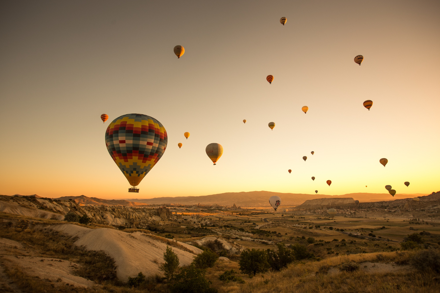 Dozens of hot air balloons at sunrise over Cappadocia landscape, Turkey | Conmigo Travel Agency