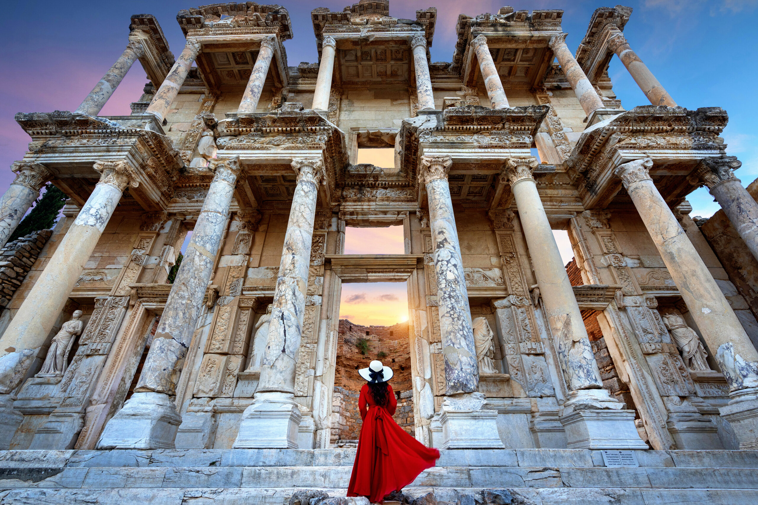 A woman in a red dress standing in front of the Celsus Library at the ancient city of Ephesus in Izmir, Turkey.